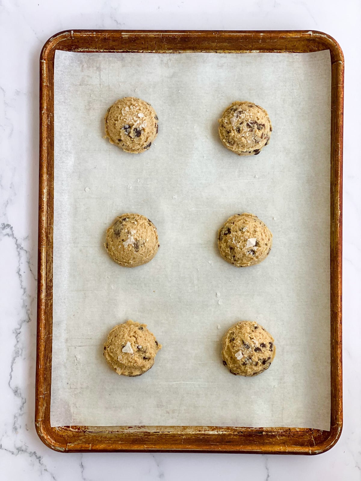 Chocolate chunk cookie dough balls on a baking sheet.