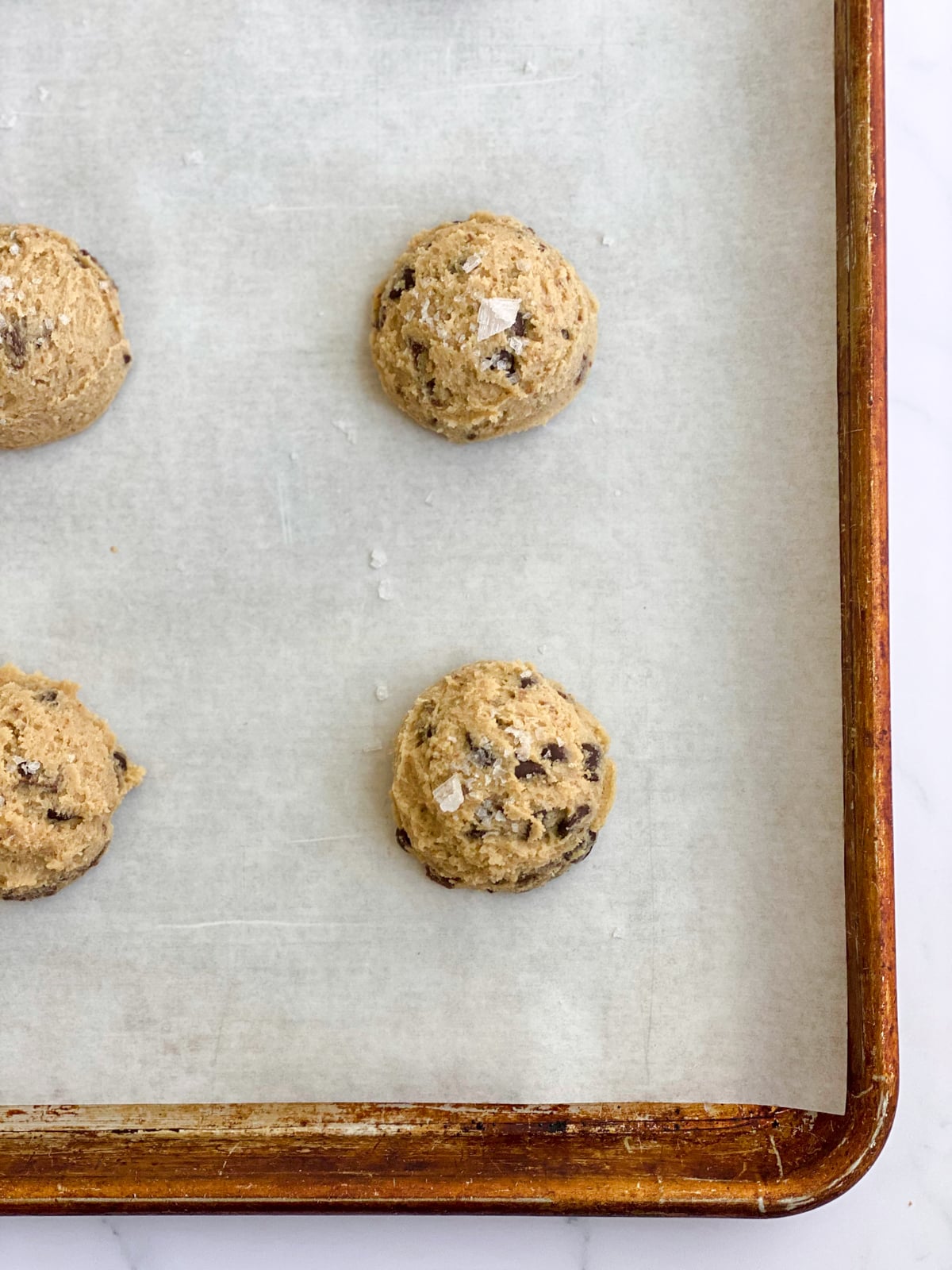 Chocolate chunk cookie dough balls on a baking sheet.