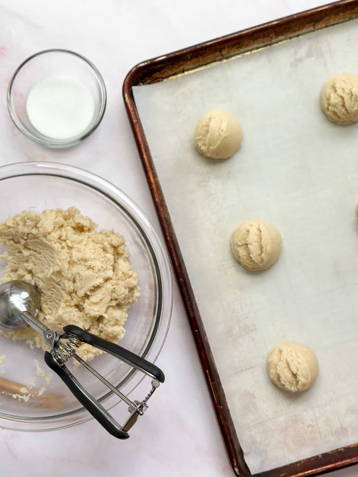 the cookie dough on a baking sheet with a bowl and cookie scoop to the side.