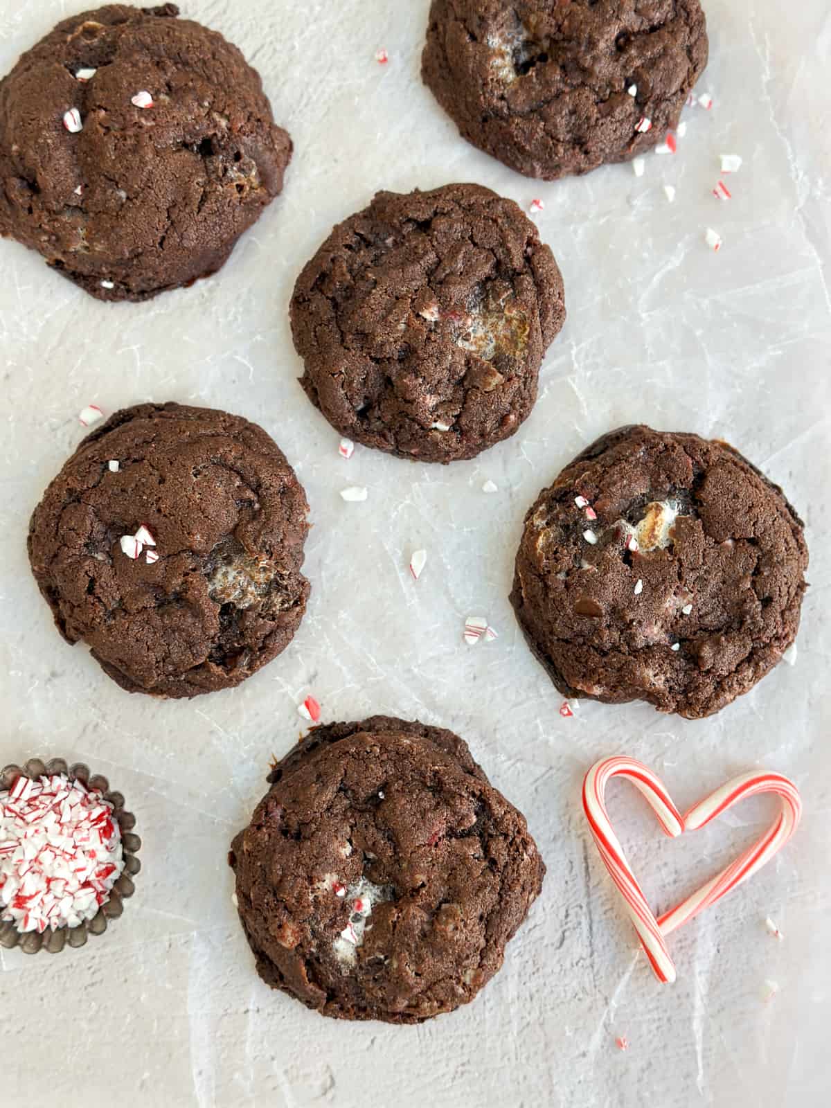 a few peppermint hot chocolate cookies with a candy cane shaped like a heart next to them.