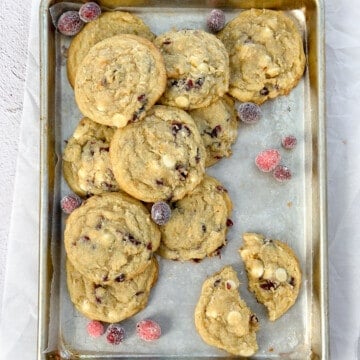 a bunch of white chocolate orange cranberry cookies on a cookie sheet with some candied cranberries.