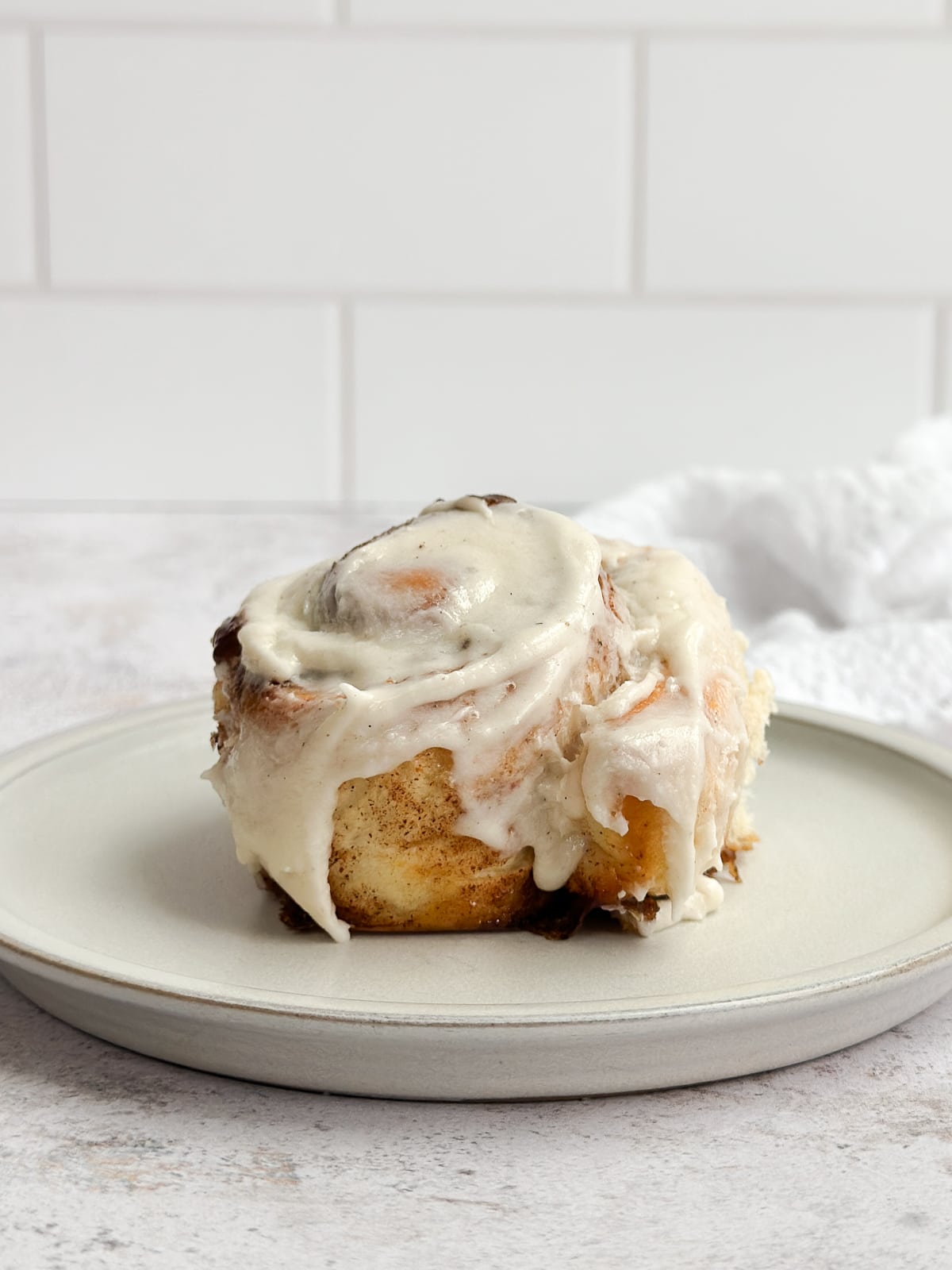 a side view of a single cinnamon roll on a plate.