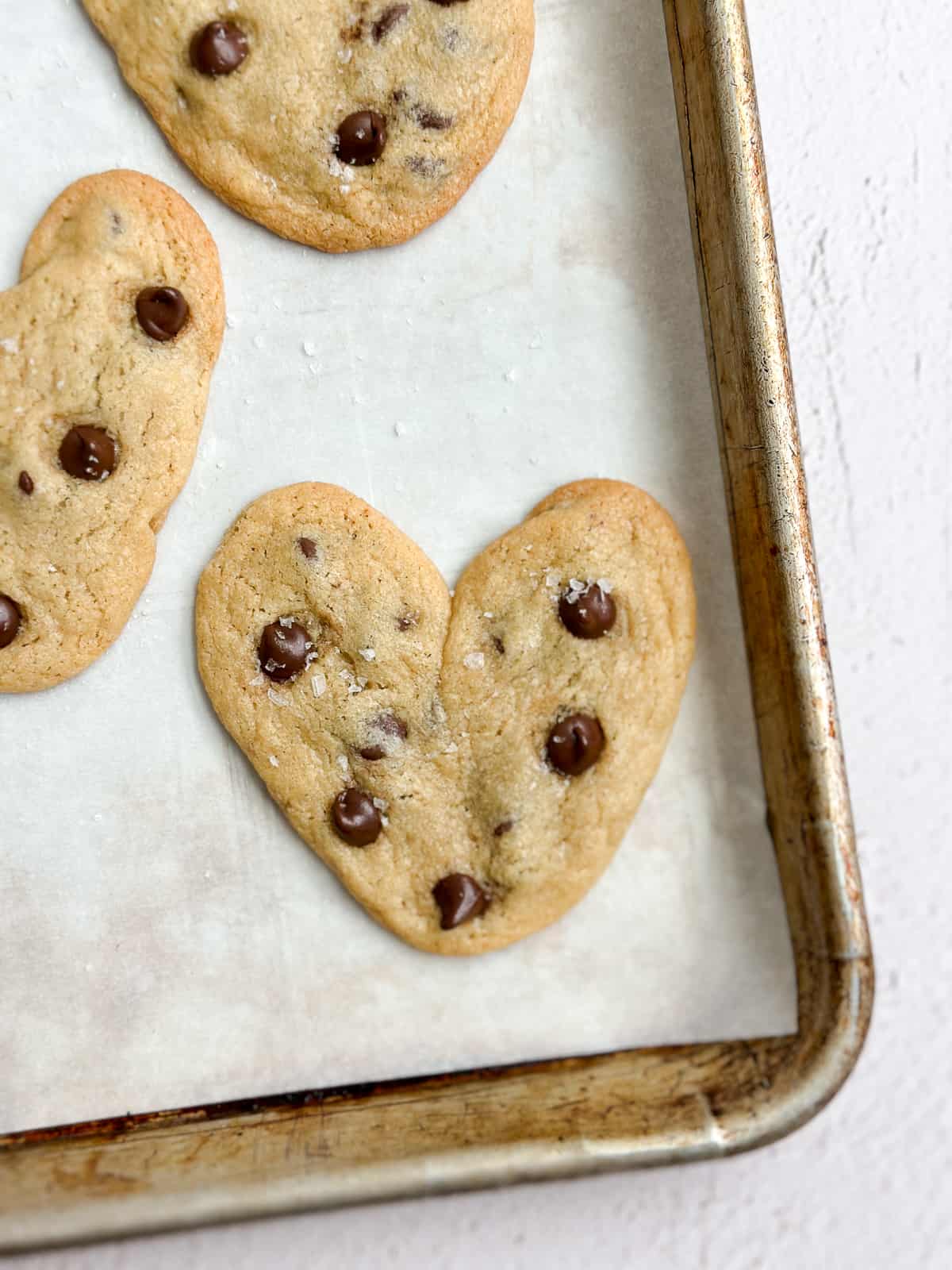 a close up of a heart shaped chocolate chip cookie on a baking sheet after baking.