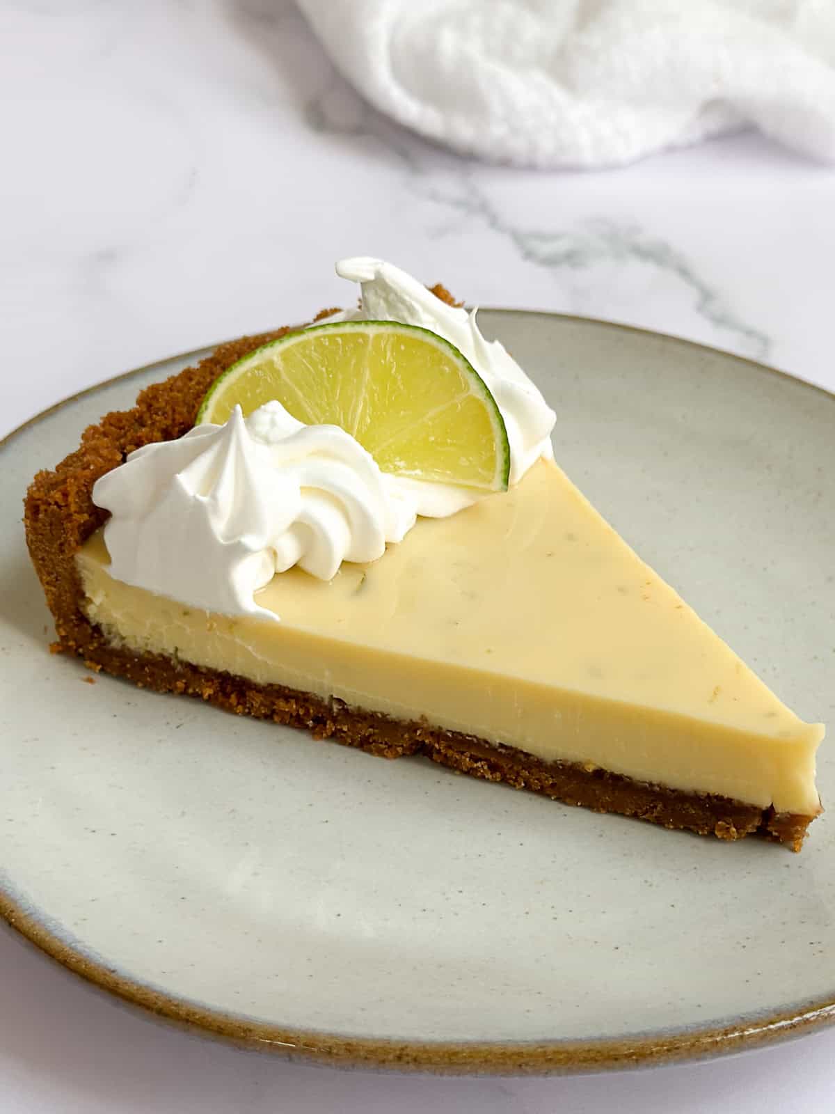 a single slice of key lime pie on a plate topped with whipped cream and a lime wedge.