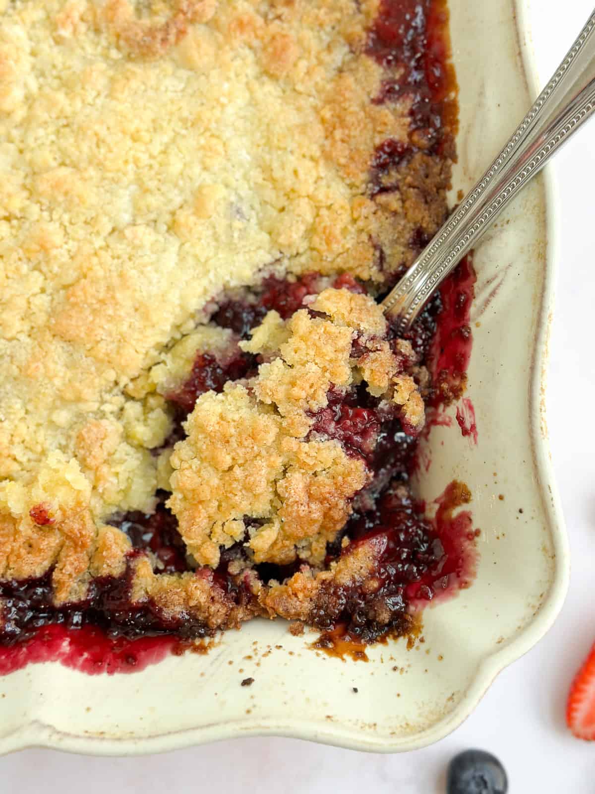 a close up of a spoon scooping out some mixed berry cobbler.