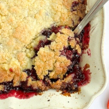 a close up of a spoon scooping out some mixed berry cobbler.