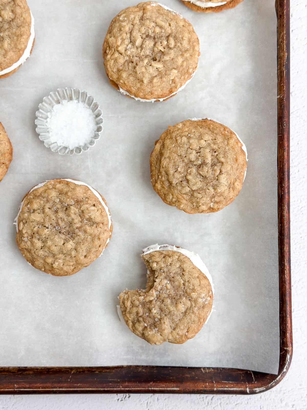 a few oatmeal cream pie cookies on a baking sheet with a bite missing from one.