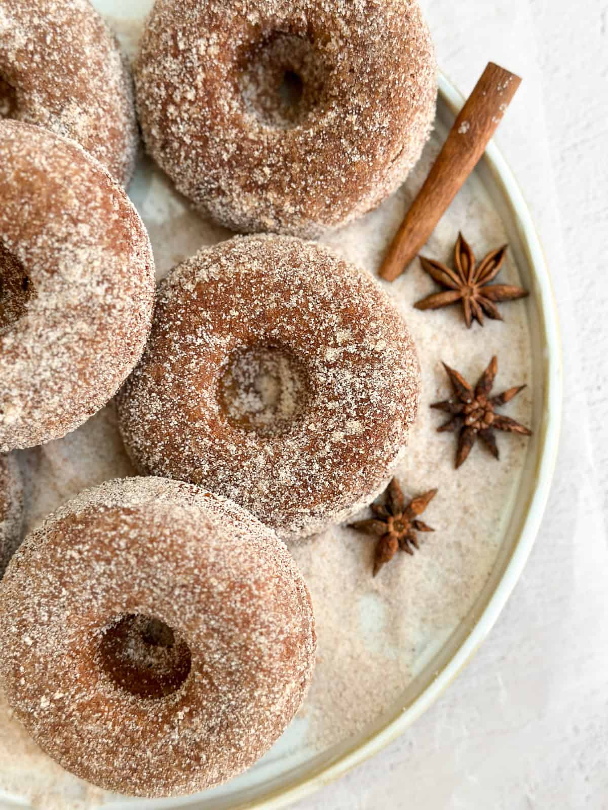 a bunch of baked apple cider donuts on a plate covered in cinnamon and sugar.