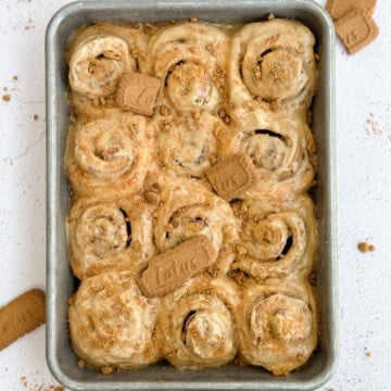 Biscoff cinnamon rolls in the baking pan with a few biscoff cookies on top.