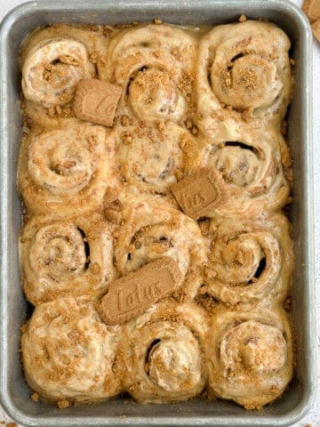 Biscoff cinnamon rolls in the baking pan with a few biscoff cookies on top.