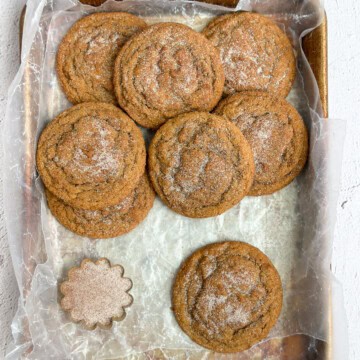 a few gingerbread snickerdoodles on a cookie sheet with cinnamon sugar in a bowl.