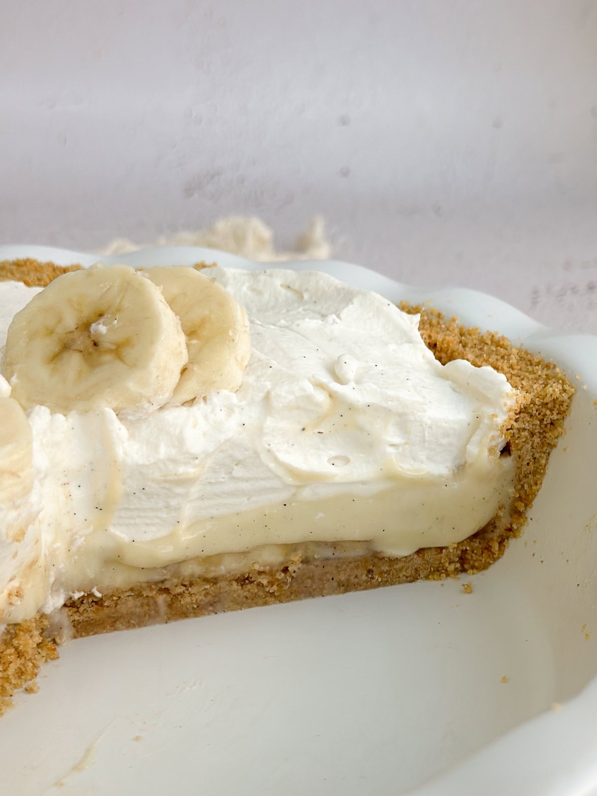 a side view of the whole banana cream pie with graham cracke4r crust cut and showing the layers.