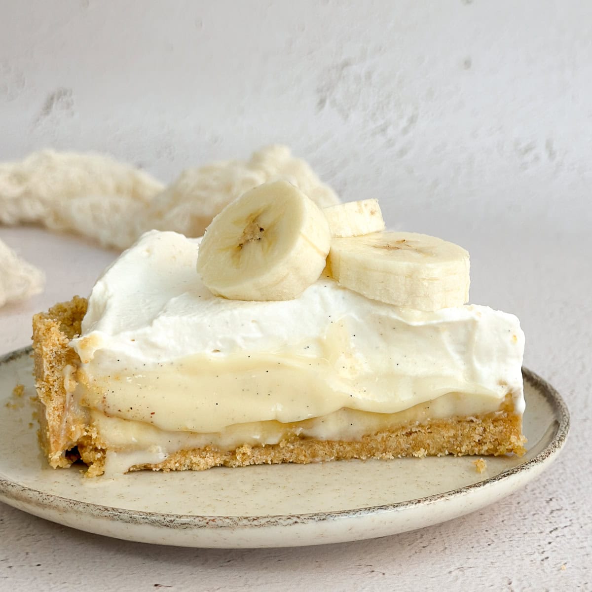 a slice of banana cream pie with graham cracker crust on a plate.