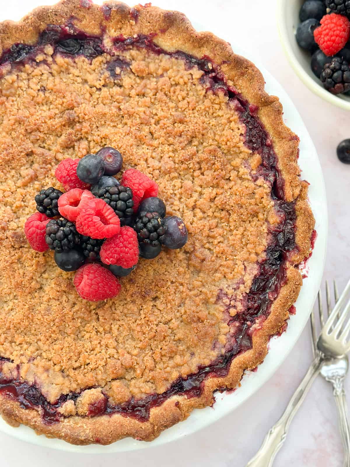 a close up of the whole mixed berry crumble pie topped with fresh berries.