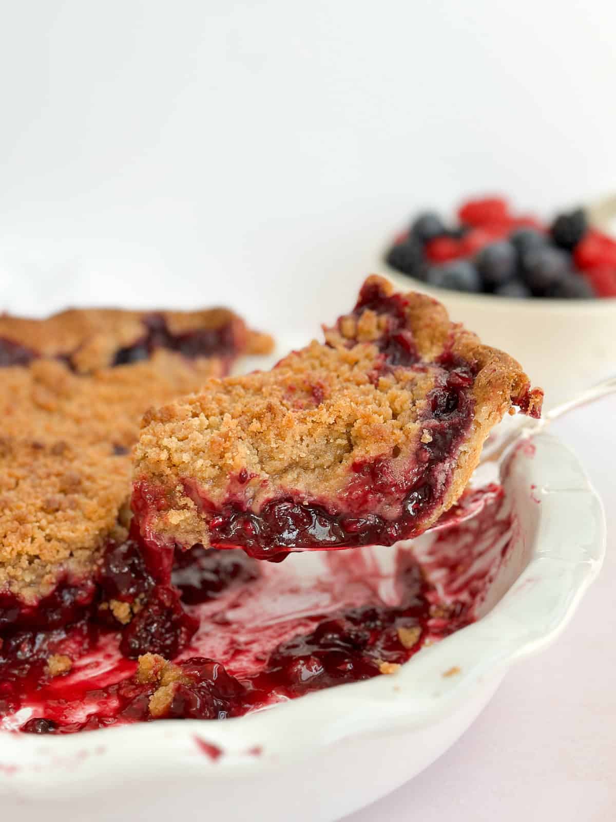 a slice of mixed berry crumble pie on a spatula coming out of the pie plate.