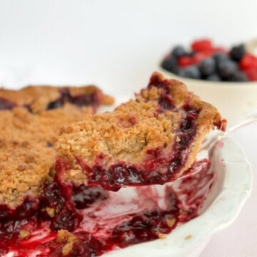 a slice of mixed berry crumble pie on a spatula coming out of the pie plate.