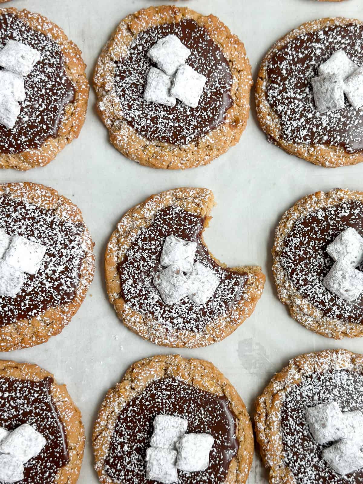 Une fournée de cookies Puppy Chow sur une plaque de cuisson avec une bouchée manquante.