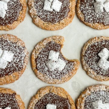 a bunch of puppy chow cookies on a baking sheet with a bite missing from one.