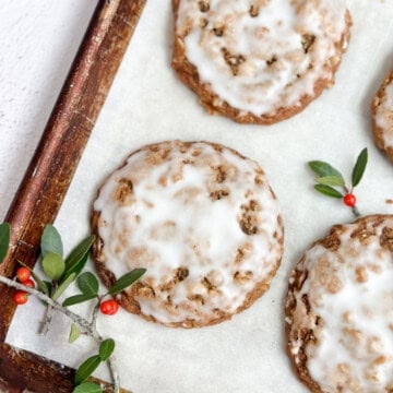 a few gingerbread oatmeal cookies on a cookie sheet with some holiday berries near them.