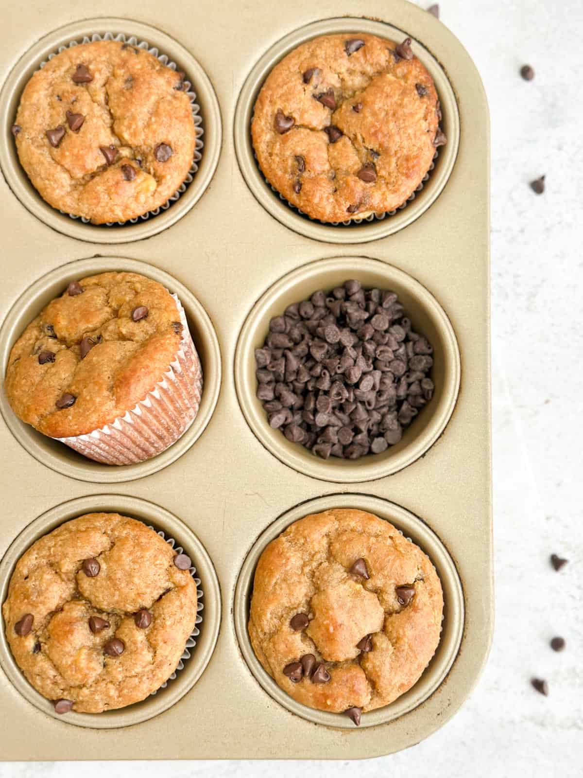 6 muffins in the muffin tin surrounded by chocolate chips.