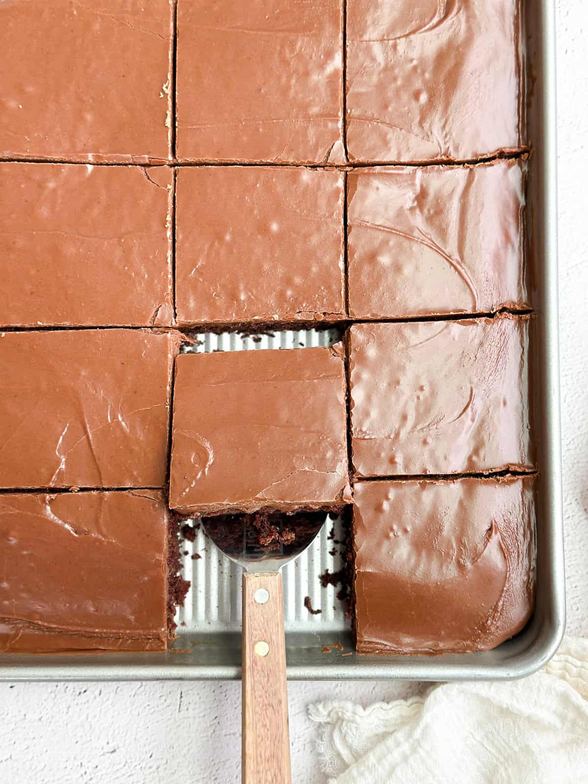a piece of chocolate buttermilk sheet cake being pulled out from a spatula.