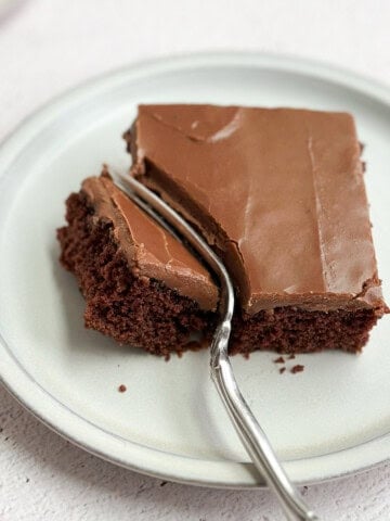 a single piece of chocolate buttermilk texas sheet cake on a plate with a fork through it.