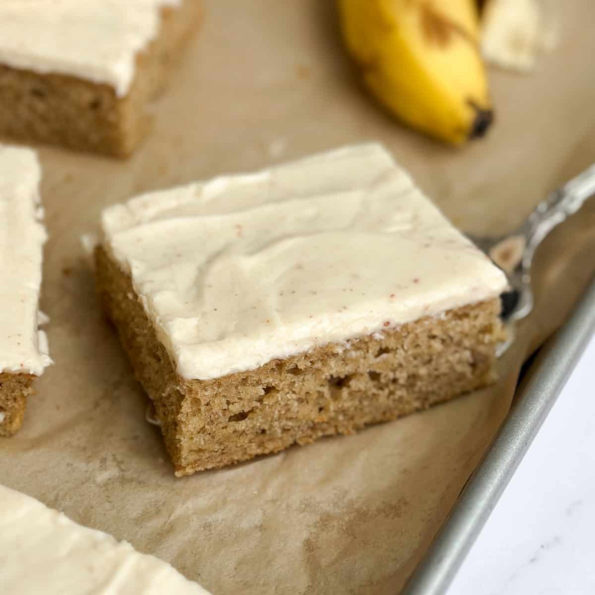 a close up of a single slice of the brown butter banana sheet cake on a sheet cake pan.