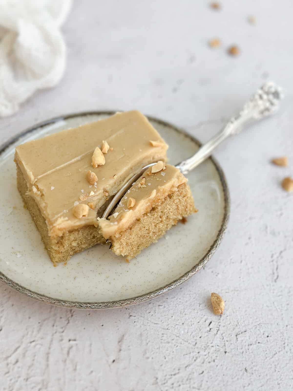 une tranche de gâteau à la crème de cacahuète avec glaçage à la crème de cacahuète, garnie de cacahuètes et de sel en flocons.