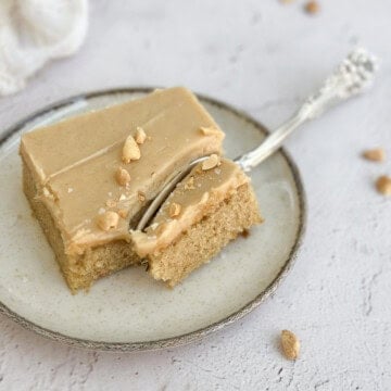 a single slice of peanut butter sheet cake with peanut butter frosting on a plate topped with peanut and flaked salt.