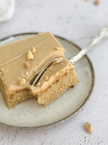 a single slice of peanut butter sheet cake with peanut butter frosting on a plate topped with peanut and flaked salt.