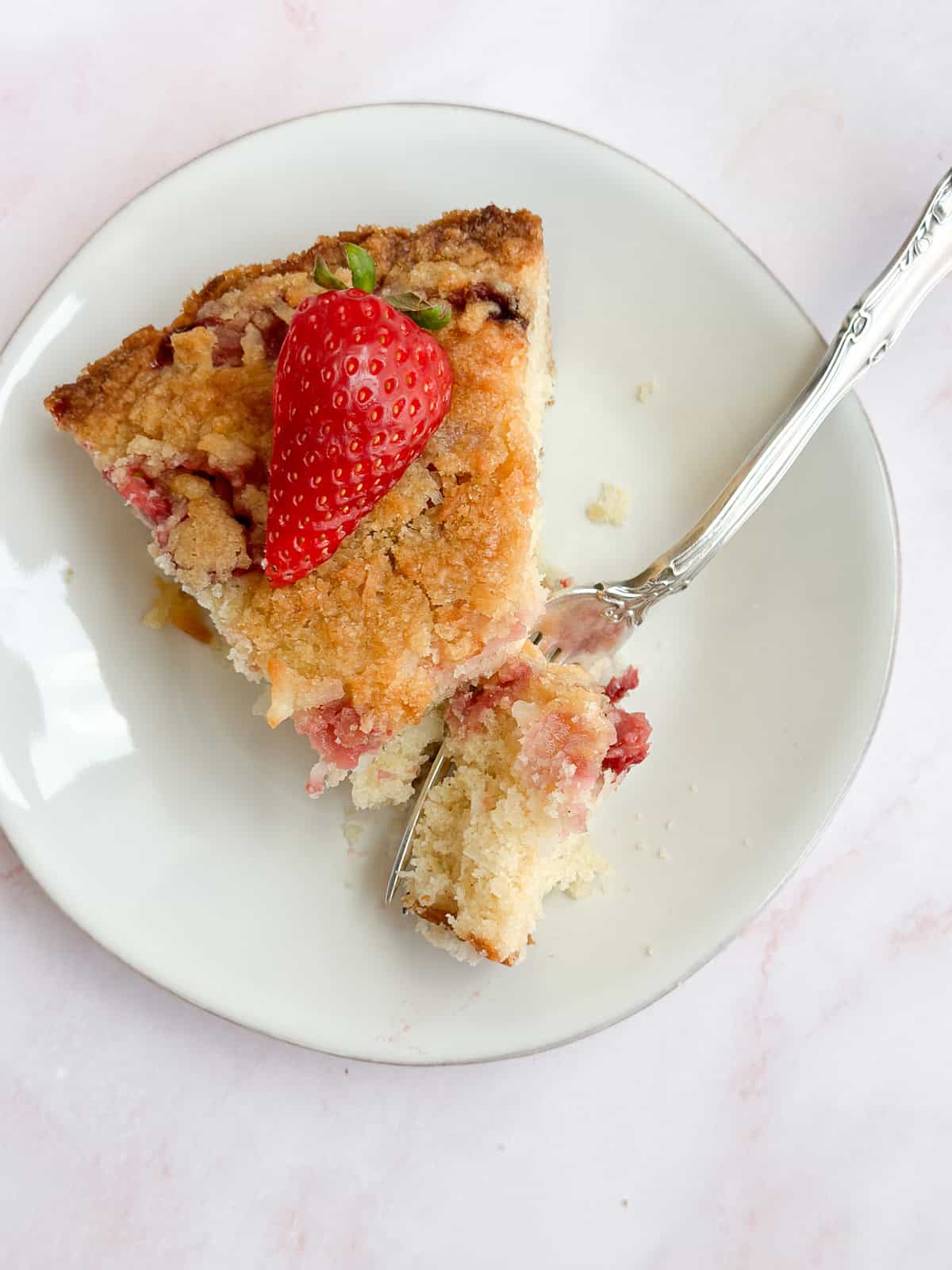une part de gâteau à la noix de coco et aux fraises sur une assiette avec une fourchette tenant une bouchée.