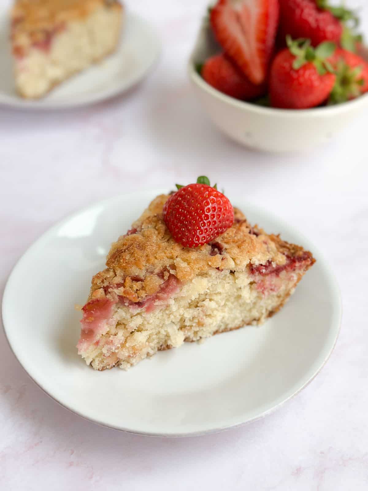a single slice of coconut strawberry cake with a fresh sliced strawberry on top.