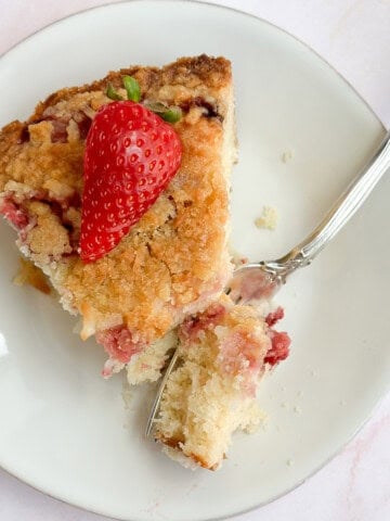 a slice of coconut strawberry cake on a plate with a fork holding a bite.