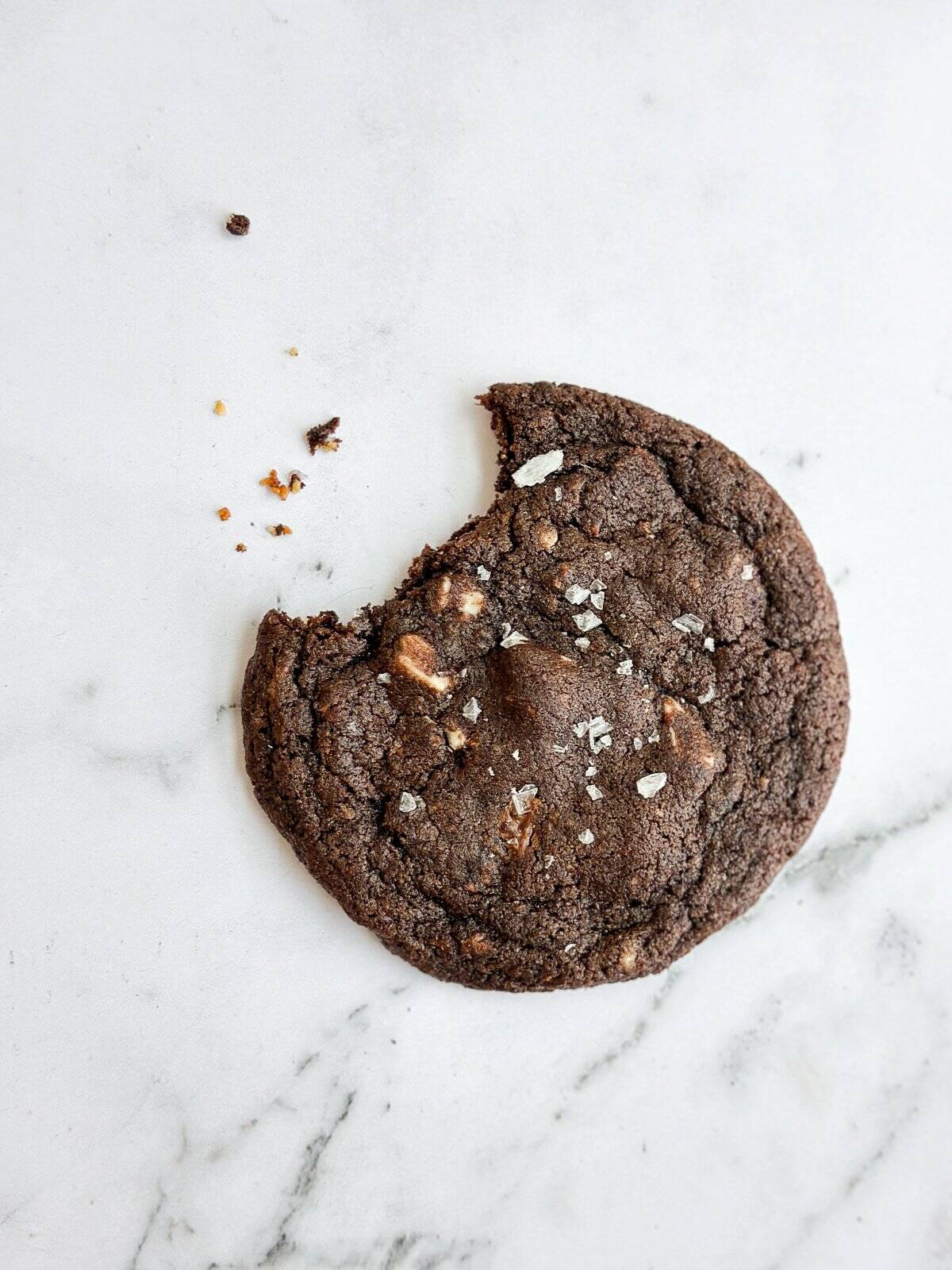 a close up of a triple chocolate cookie with a bite missing and some crumbs.