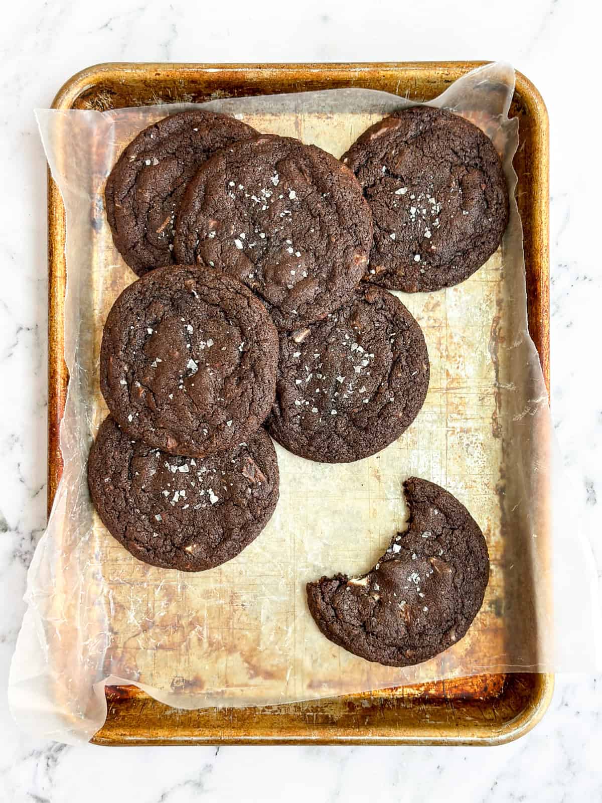 a few triple chocolate cookies on a cookie sheet with a bite missing from one.