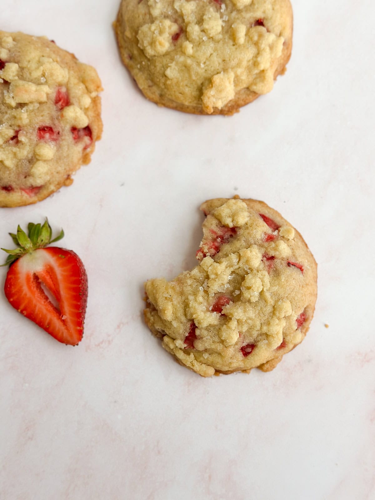 Un biscuit aux fraises crumble avec une bouchée manquante et quelques autres biscuits autour.