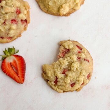 one strawberry crumble cookie with a bite missing and a few other cookies around.