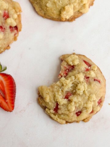 one strawberry crumble cookie with a bite missing and a few other cookies around.