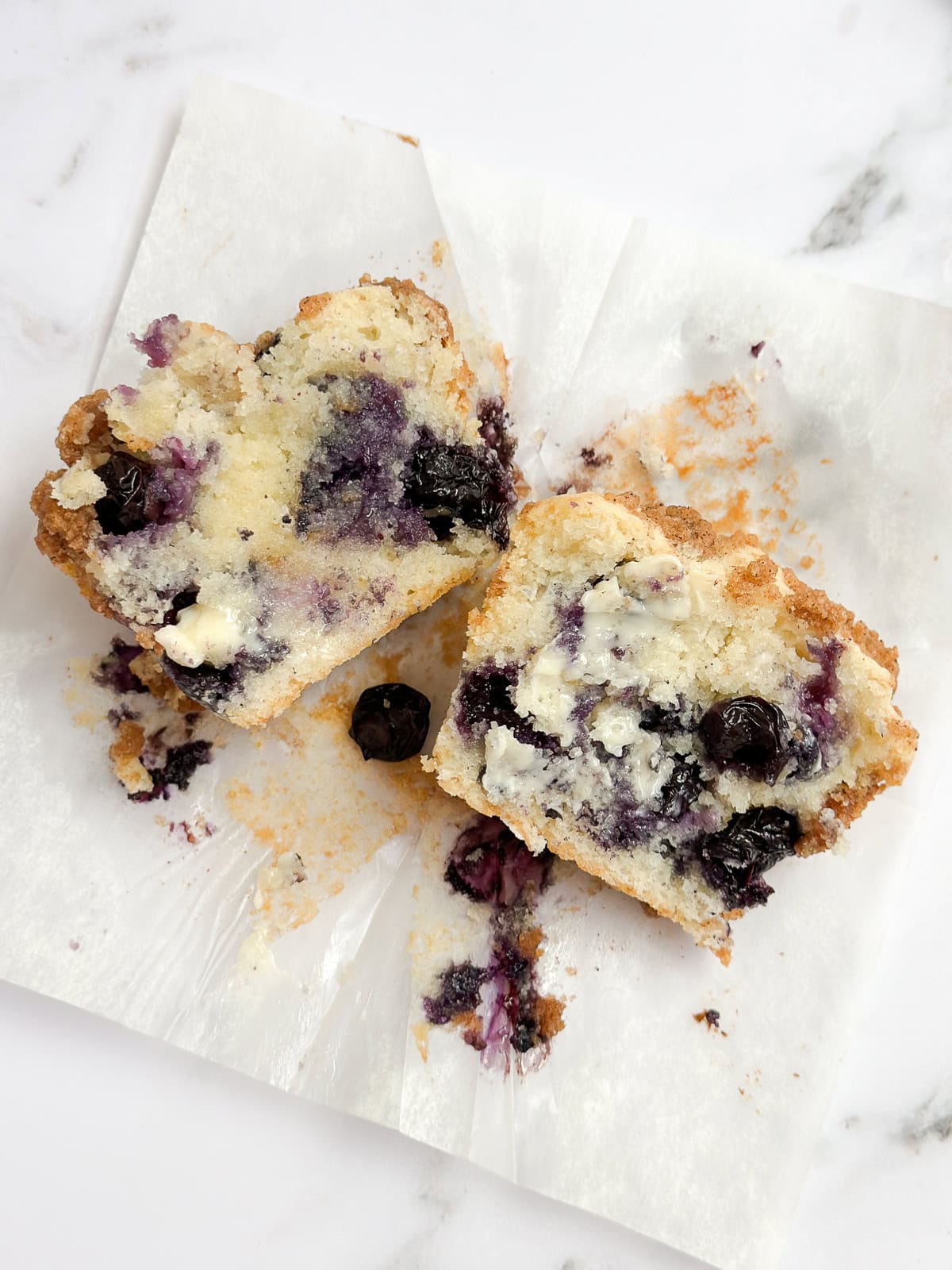 a blueberry coffee cake muffin cut in half so you can see all the blueberries inside.
