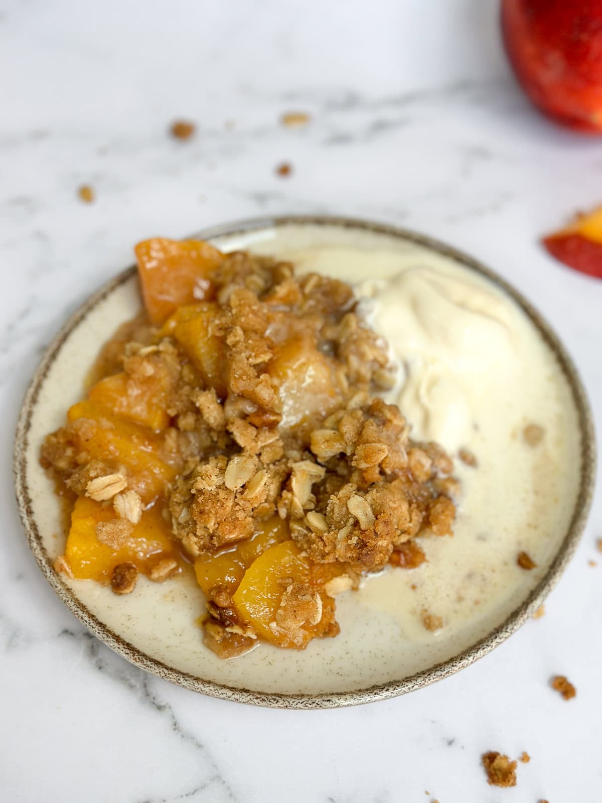 crumble de pêches au beurre noisette sur une assiette avec de la glace à la vanille.