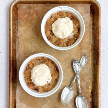 two mini individual peach cobblers on a baking sheet with two spoons.