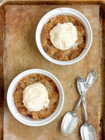 two mini individual peach cobblers on a baking sheet with two spoons.