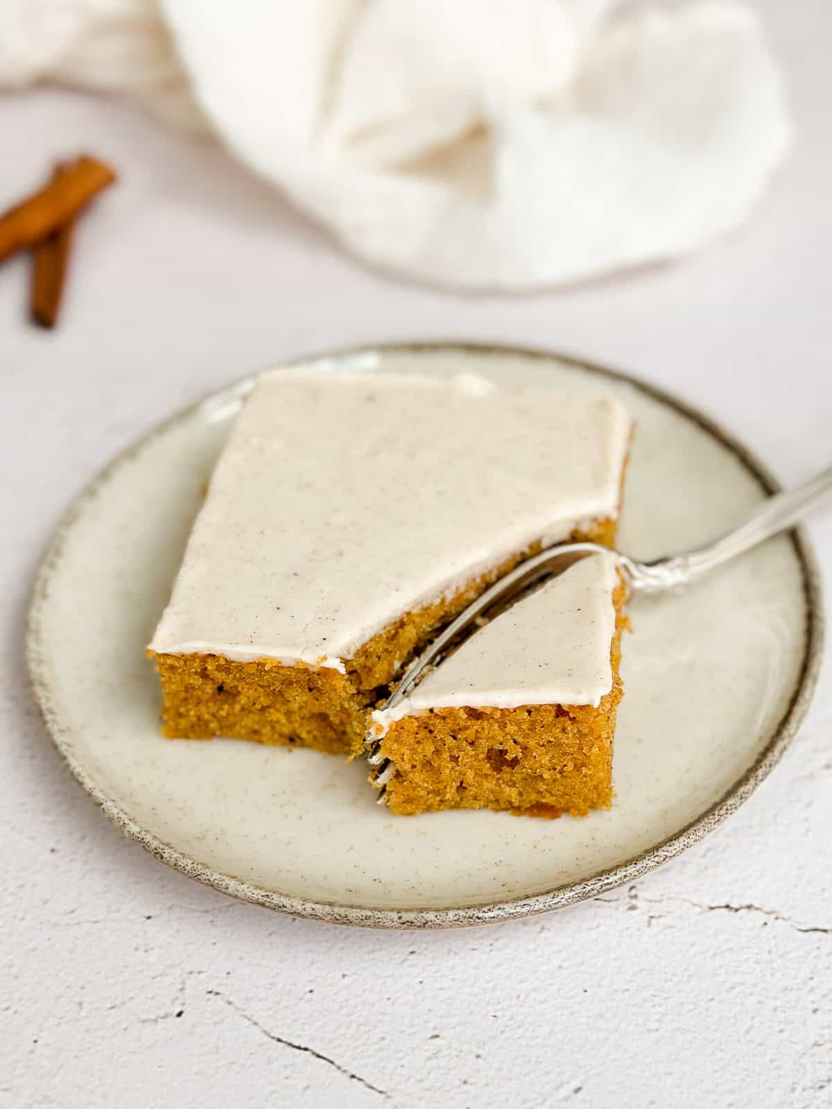 Un morceau de barres de citrouille avec glaçage au fromage à la crème à la cannelle sur une assiette avec une fourchette.