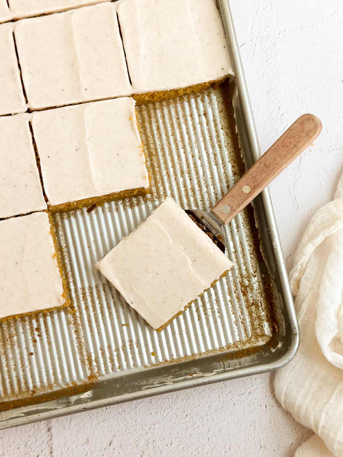 the pumpkin bars cut up on the sheet pan and a spatula holding a single piece.
