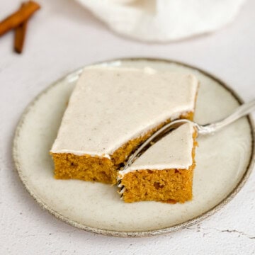 a piece of the pumpkin bars with cinnamon cream cheese frosting on a plate with a fork in it.