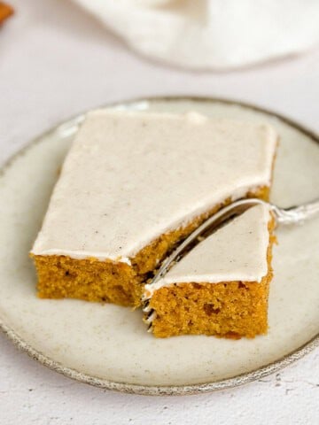 a piece of the pumpkin bars with cinnamon cream cheese frosting on a plate with a fork in it.
