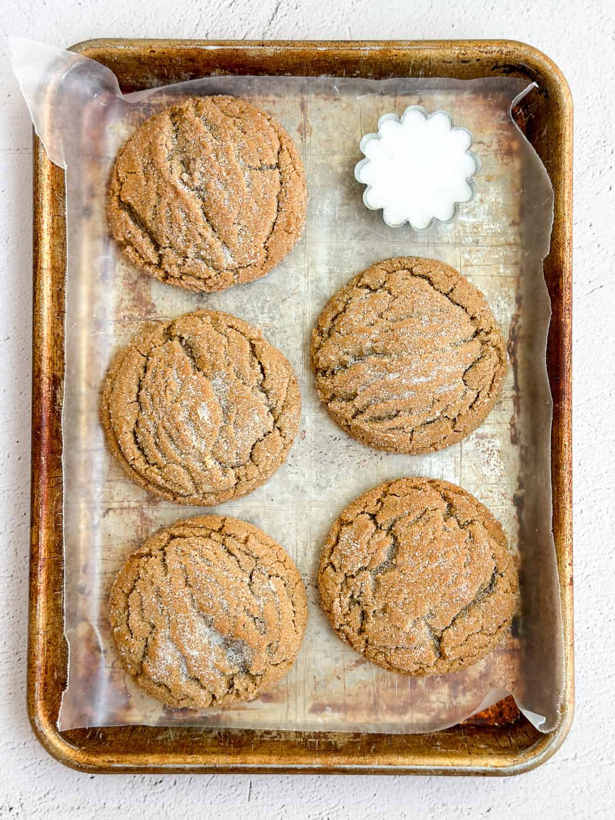 a few chewy ginger molasses cookies on a cookie sheet with some sugar on the side.