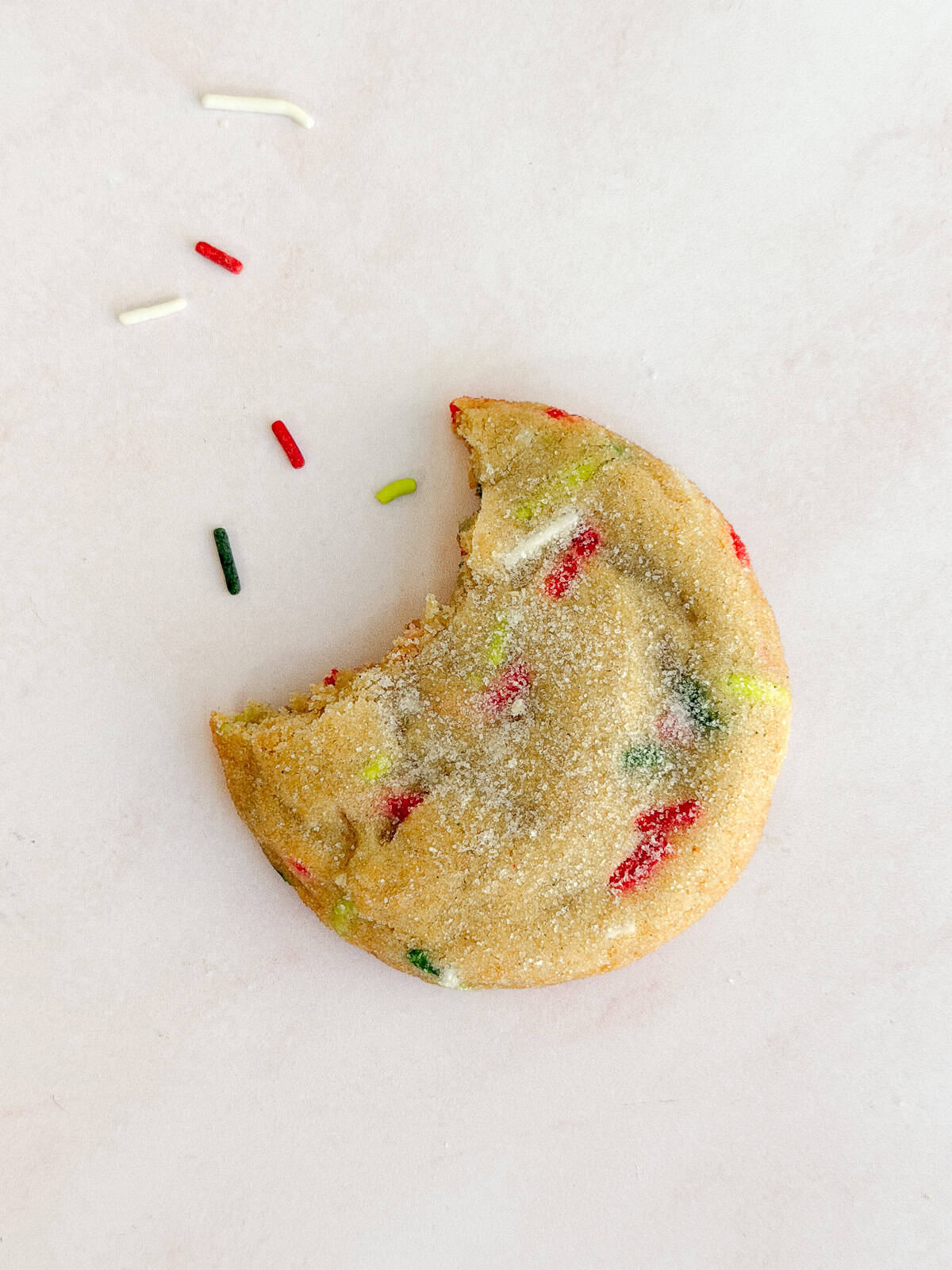 a single Christmas sprinkle sugar cookie with a bite missing and sprinkles coming out.