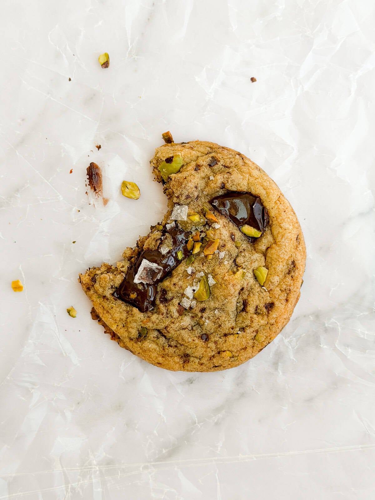 a close up of a single pistachio chocolate chip cookie with a bite missing.