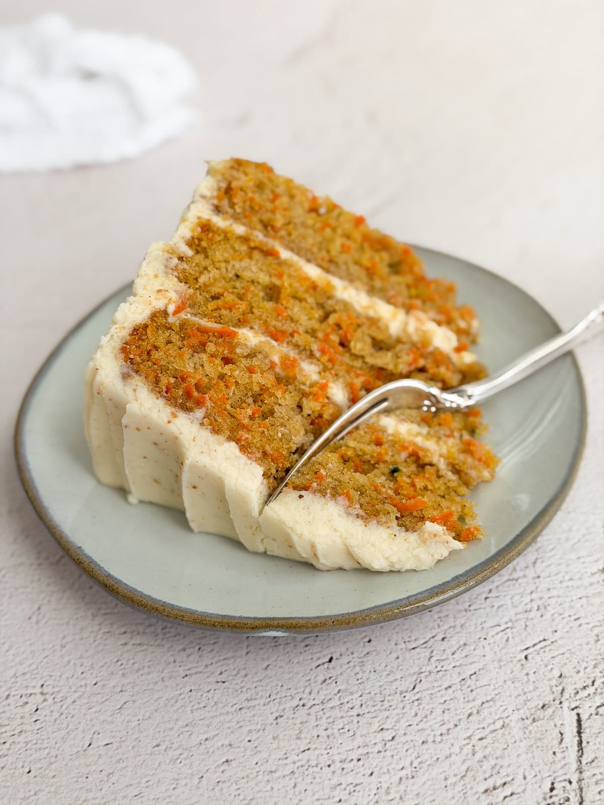 a slice of the carrot cake with brown butter cream cheese frosting on a plate.
